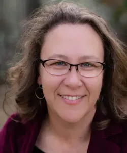 Woman with brown hair and glasses smiling at the camera.